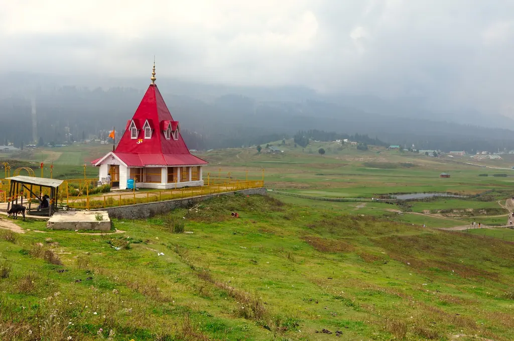 The red-roofed Maharani Temple overlooking the green meadow bowl of Gulmarg, forested hills veiled in mist