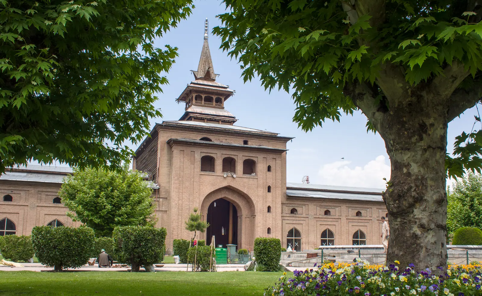 The pagoda-style spire of Jamia Masjid, Srinagar's Grand Mosque, framed by chinar leaves and spring flowerbeds