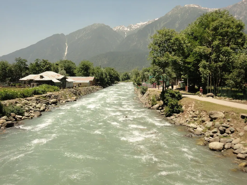 The glacial Lidder river rushing through Pahalgam town, pine-covered mountains and snow peaks behind