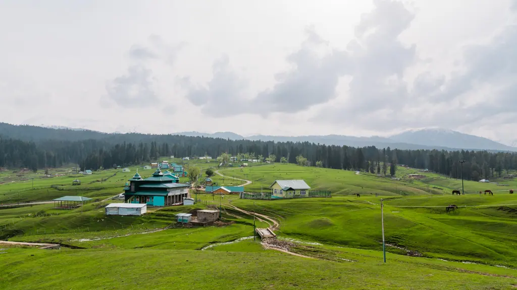 The rolling green meadows of Yusmarg dotted with huts and grazing horses, framed by pine forest