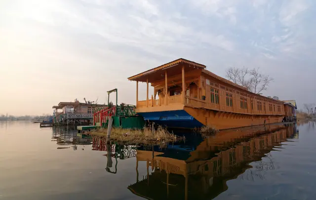 Carved cedar-wood houseboat moored on Dal Lake, Srinagar, reflected in calm morning water