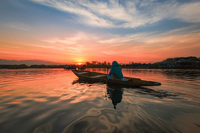 Lone shikara on Dal Lake at sunset, sky and rippling water glowing orange and pink